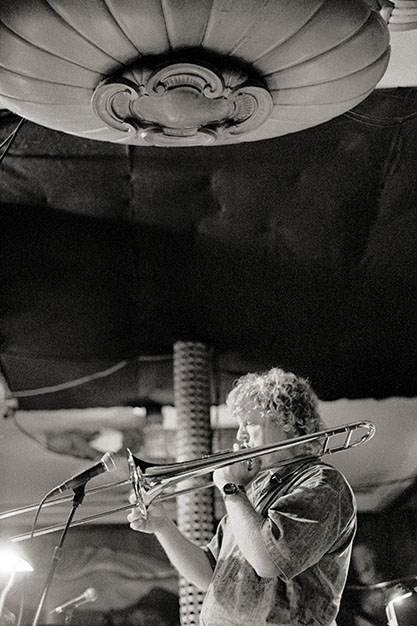 A man plays a trombone. Some architectural elements of the inside of the club are visible.