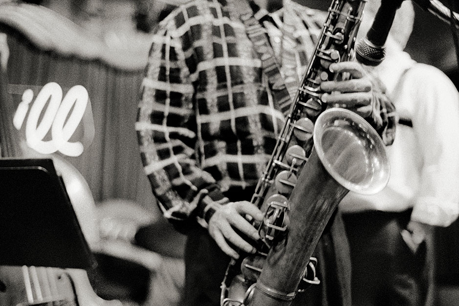 A saxophonist, wearing a plaid shirt, takes a solo.