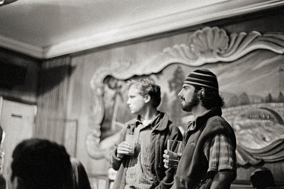 Two men stand near the stage, listening and watching.