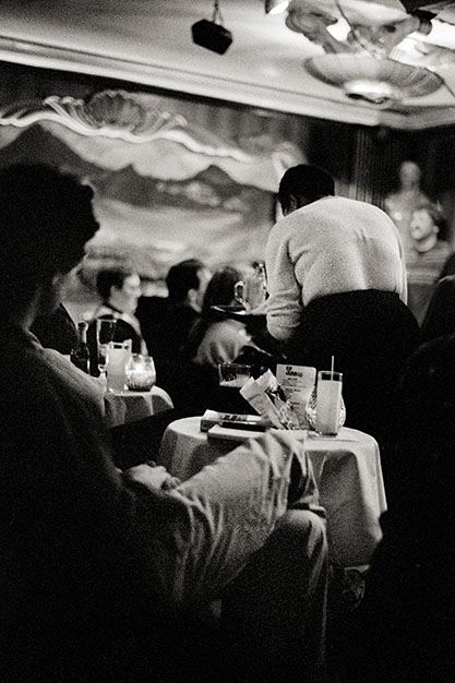 A man leans back listening while a waitress works at a nearby table.